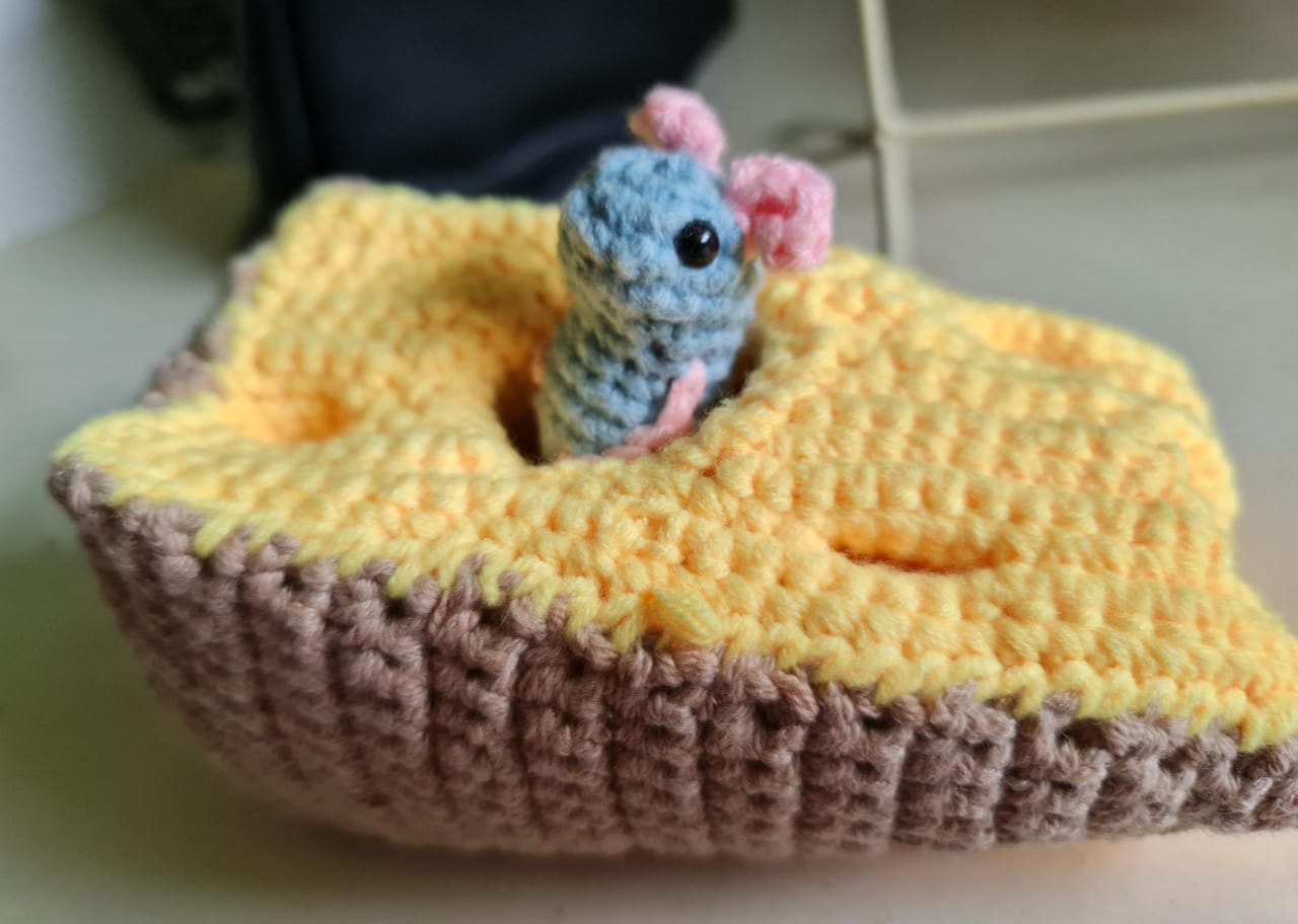 A crochet mouse poking out of a crochet cheese.