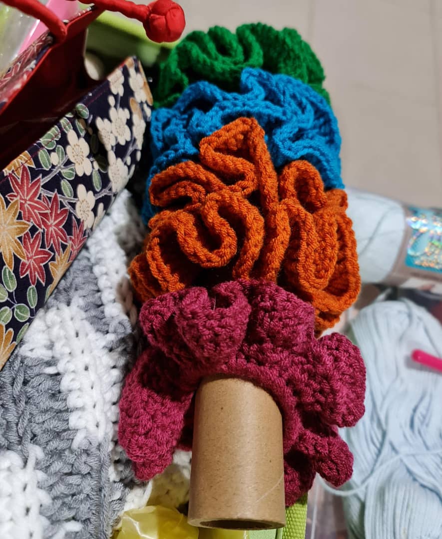 A cardboard tube with 3 hair scrunchies made of crochet on it